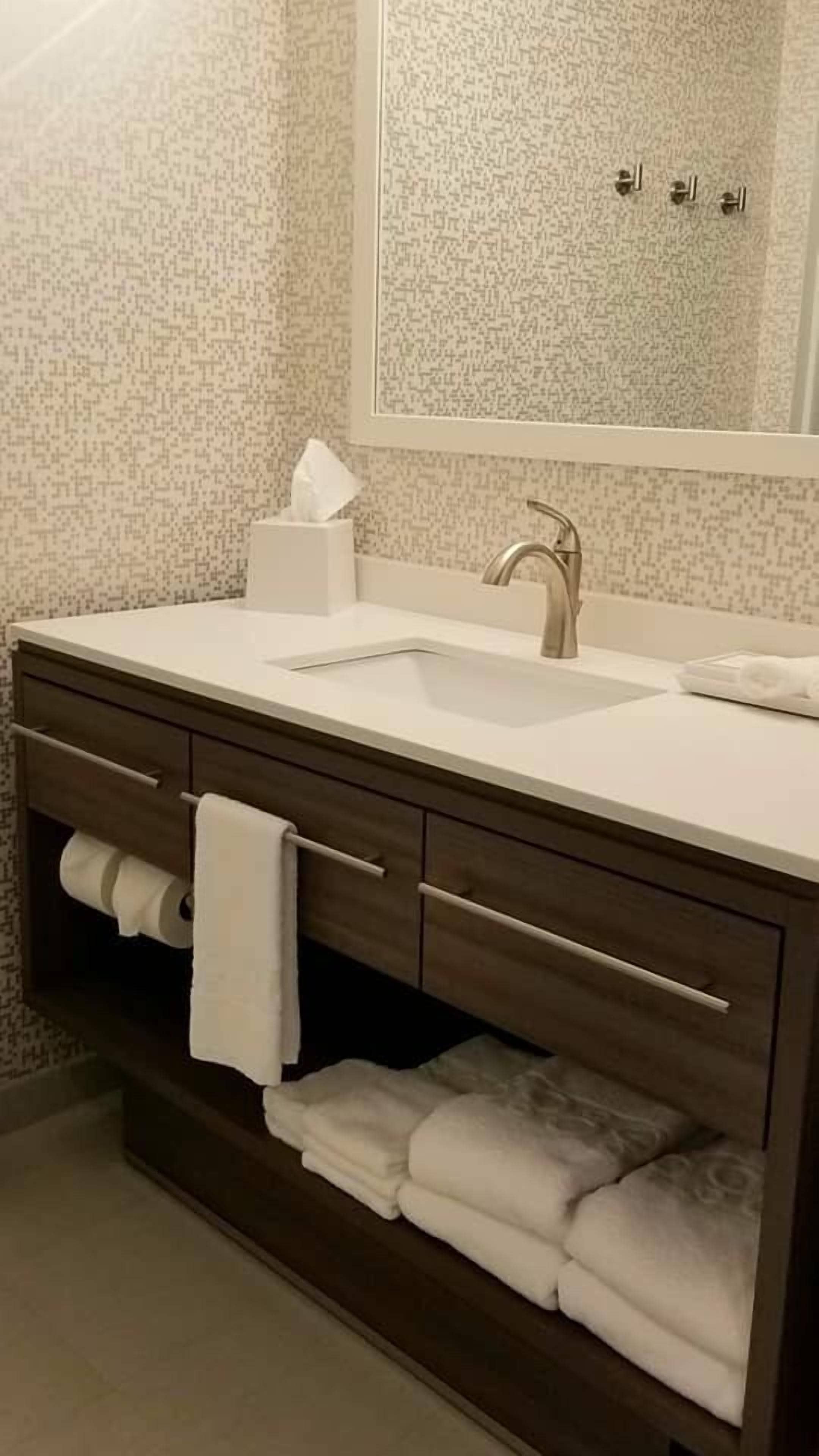 Un baño con lavamanos blanco, tocador de madera oscura y un espejo sobre el lavamanos.