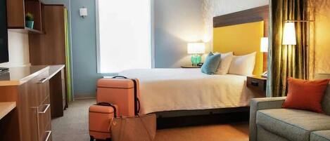 A hotel room with a bed, bedside table, lamp, and a suitcase.