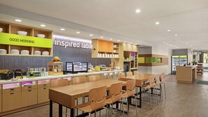 A modern cafe with multiple seating areas, a counter with a menu display, and a 'Good Morning' sign. - Home2 Suites by Hilton Fernandina Beach Amelia Island, FL (Fernandina Beach)