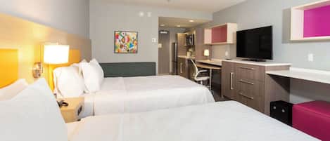 A hotel room with two beds, a desk, a television, and a kitchenette.