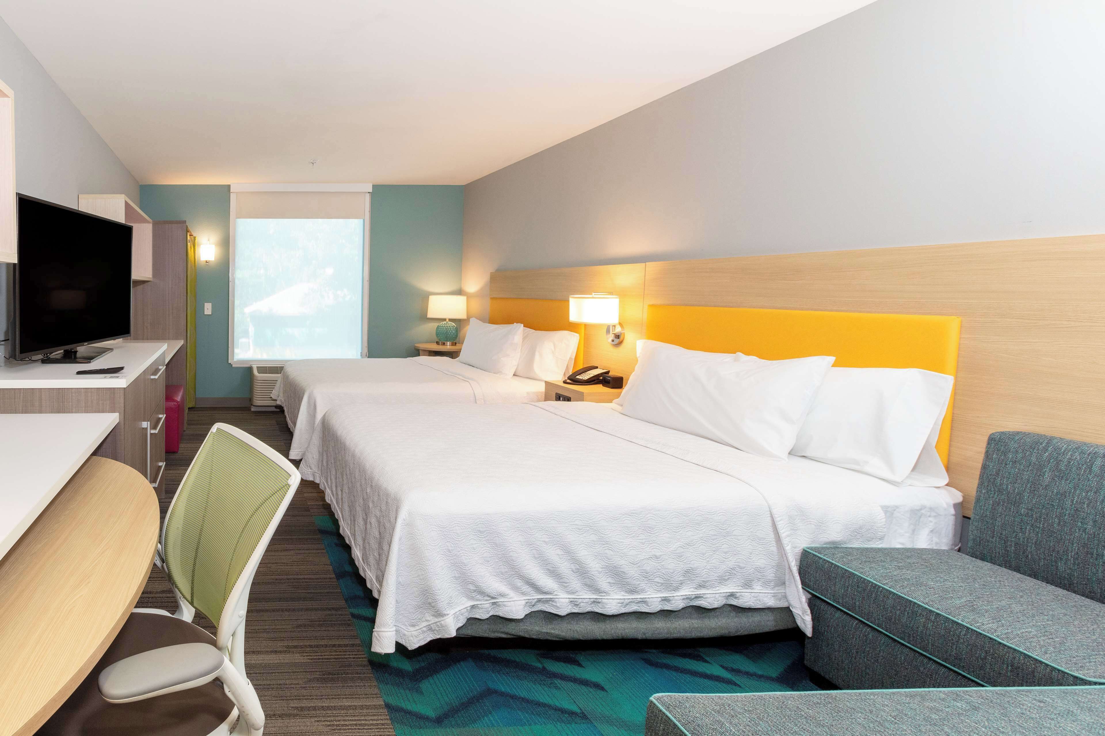 Habitación de hotel con dos camas, un escritorio con televisor, una silla y un sofá.