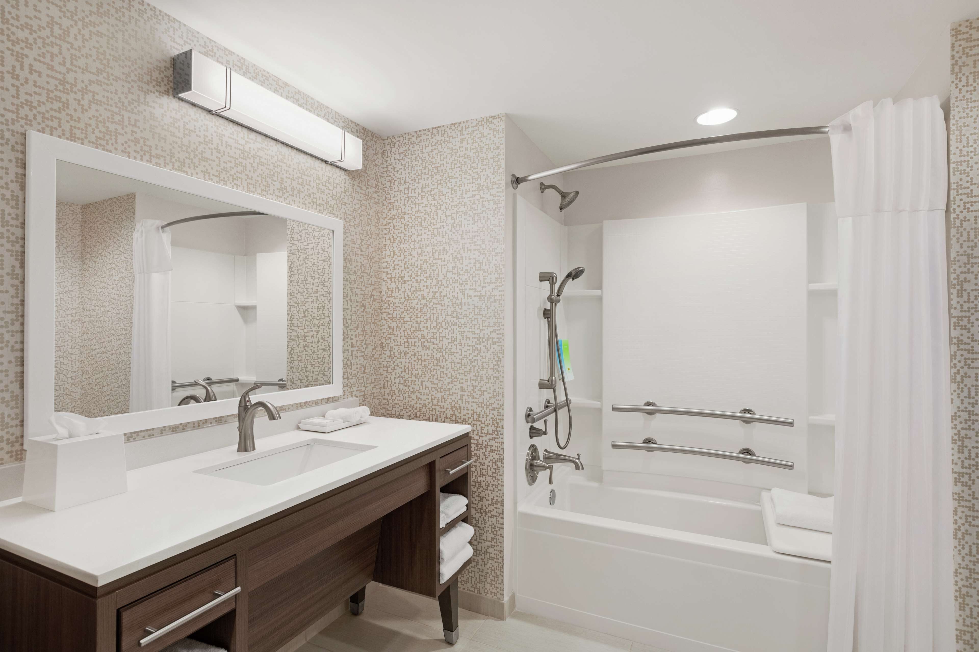 Une salle de bain moderne avec deux lavabos, un grand miroir, une douche avec un pommeau de douche amovible et une baignoire.