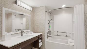 A modern bathroom with two sinks, a large mirror, a shower with a handheld showerhead, and a bathtub.