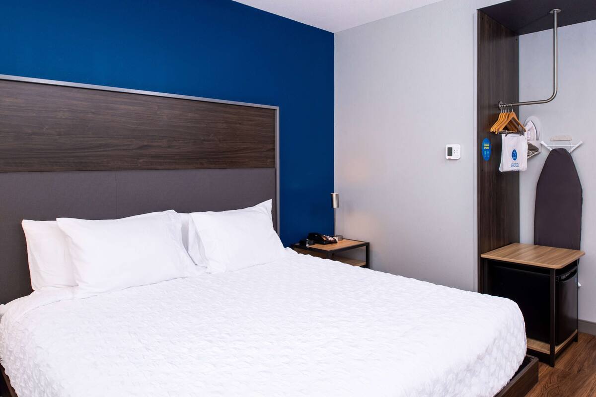 A neatly made bed with white linens in a room with a blue accent wall and a wooden headboard.