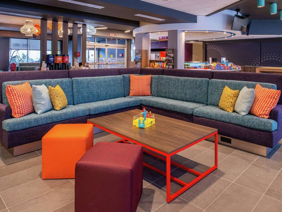 Un área de descanso moderna con un sofá modular, una mesa de centro de madera y un reposapiés naranja.