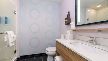 Un baño moderno con cabina de ducha de vidrio, inodoro y lavabo con tocador de madera.