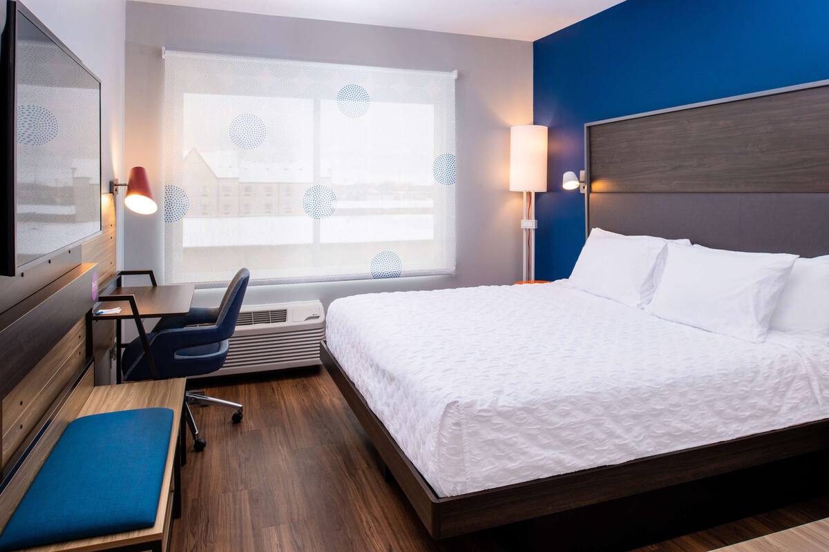 A hotel room with a bed, desk, chair, and a large window with a view.
