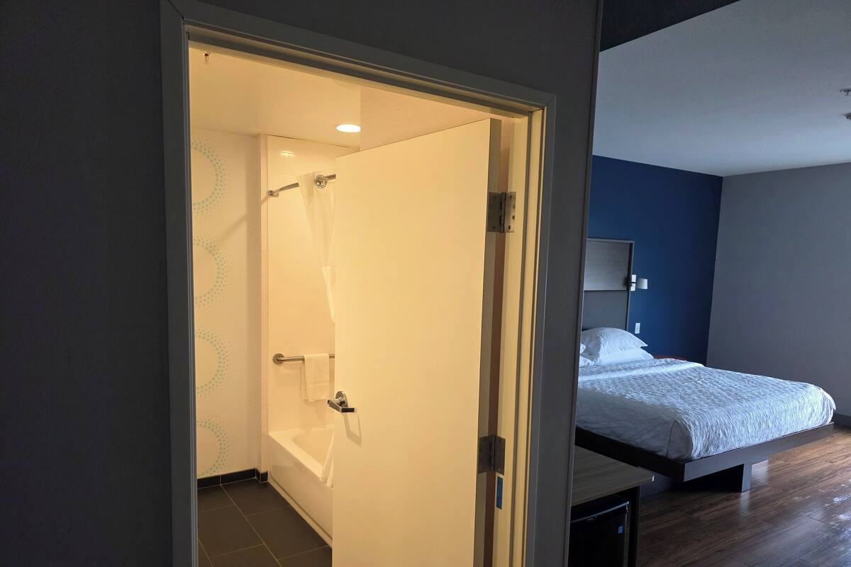 A modern bedroom with a large bed, a built-in bench, and a shower area.