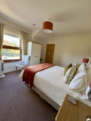 A hotel room with a bed, a chair, a desk, a window with curtains, a door, and a ceiling light. - Mourne Country House (Newry)