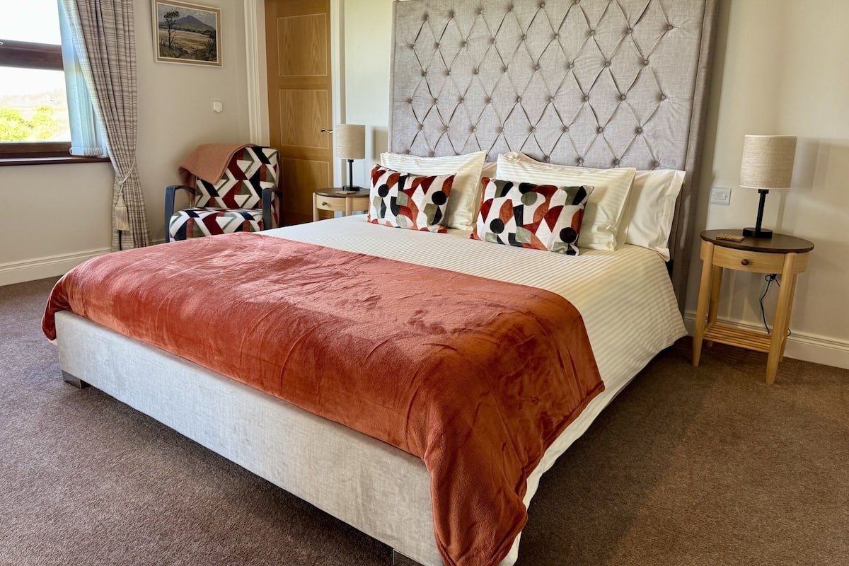 A neatly made bed with a red blanket, a tufted headboard, and patterned pillows.