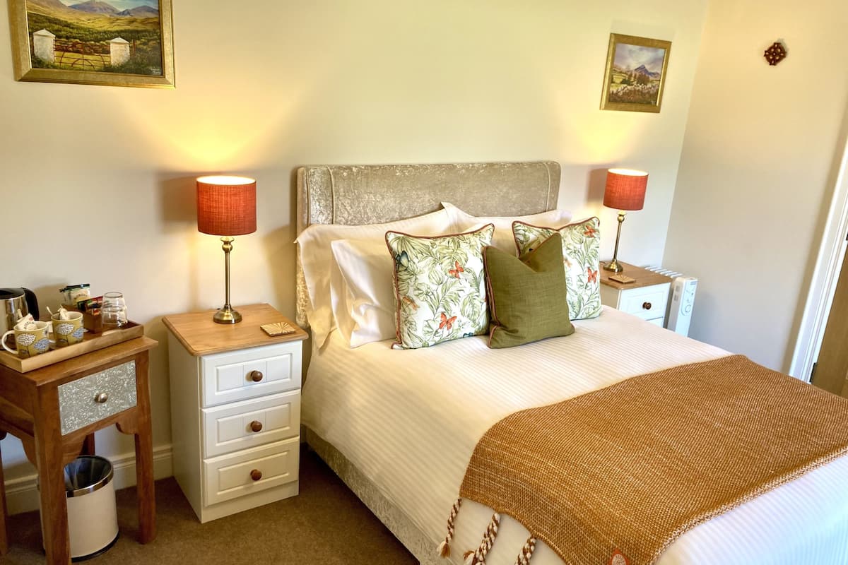 A neatly arranged bedroom with a bed, two bedside tables, a nightstand, a small wooden cabinet, and two wall-mounted lamps.