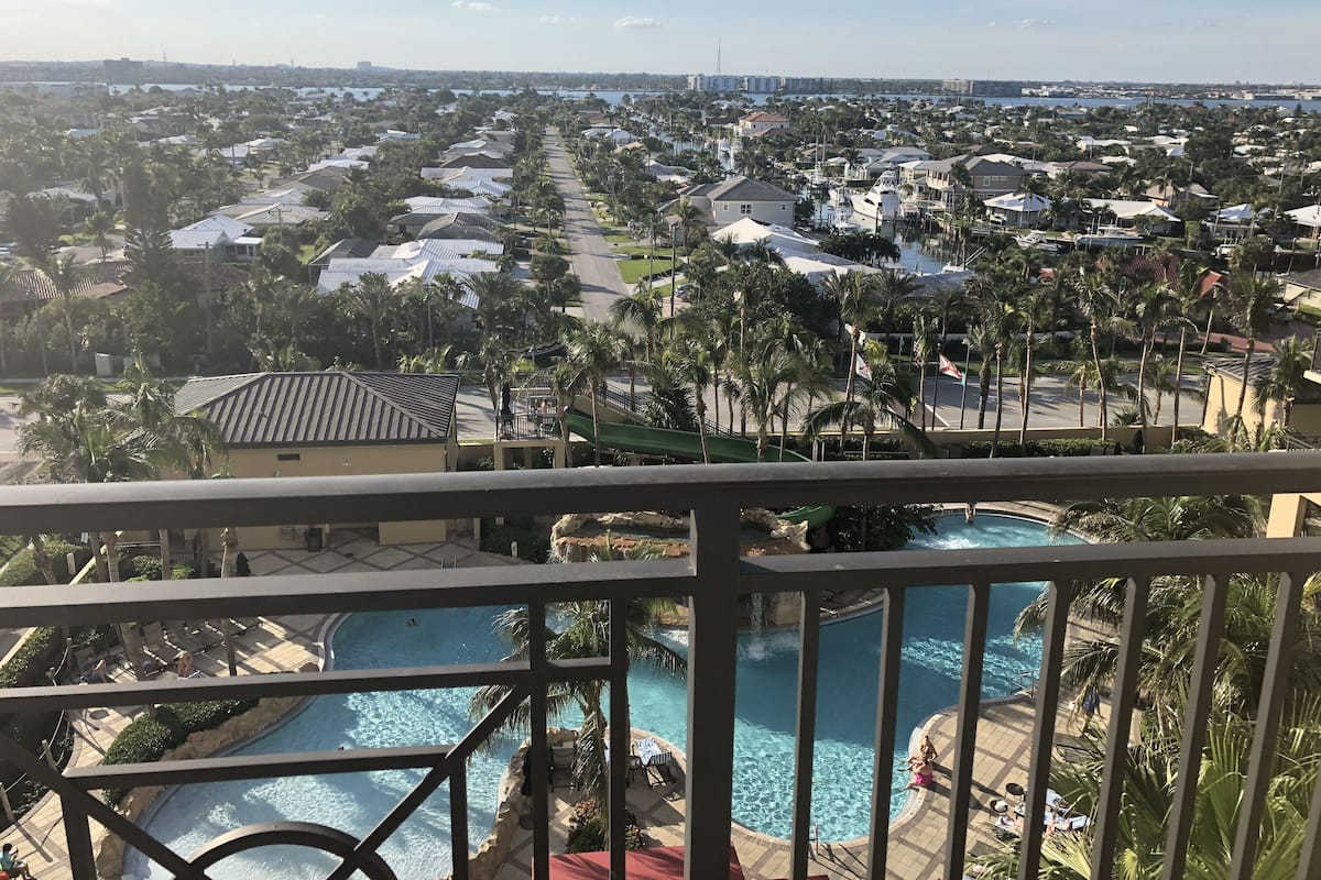 A resort with multiple swimming pools, palm trees, and a view of the surrounding residential area.