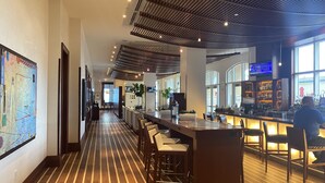 A hotel lobby with a long reception desk, bar area, and seating.