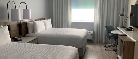 A hotel room with two beds, a desk, a chair, a TV, and a window with curtains.