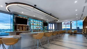 A modern bar area with a long counter, multiple stools, and a variety of bottles. - Wyndham Garden Miami International Airport (Miami Springs)