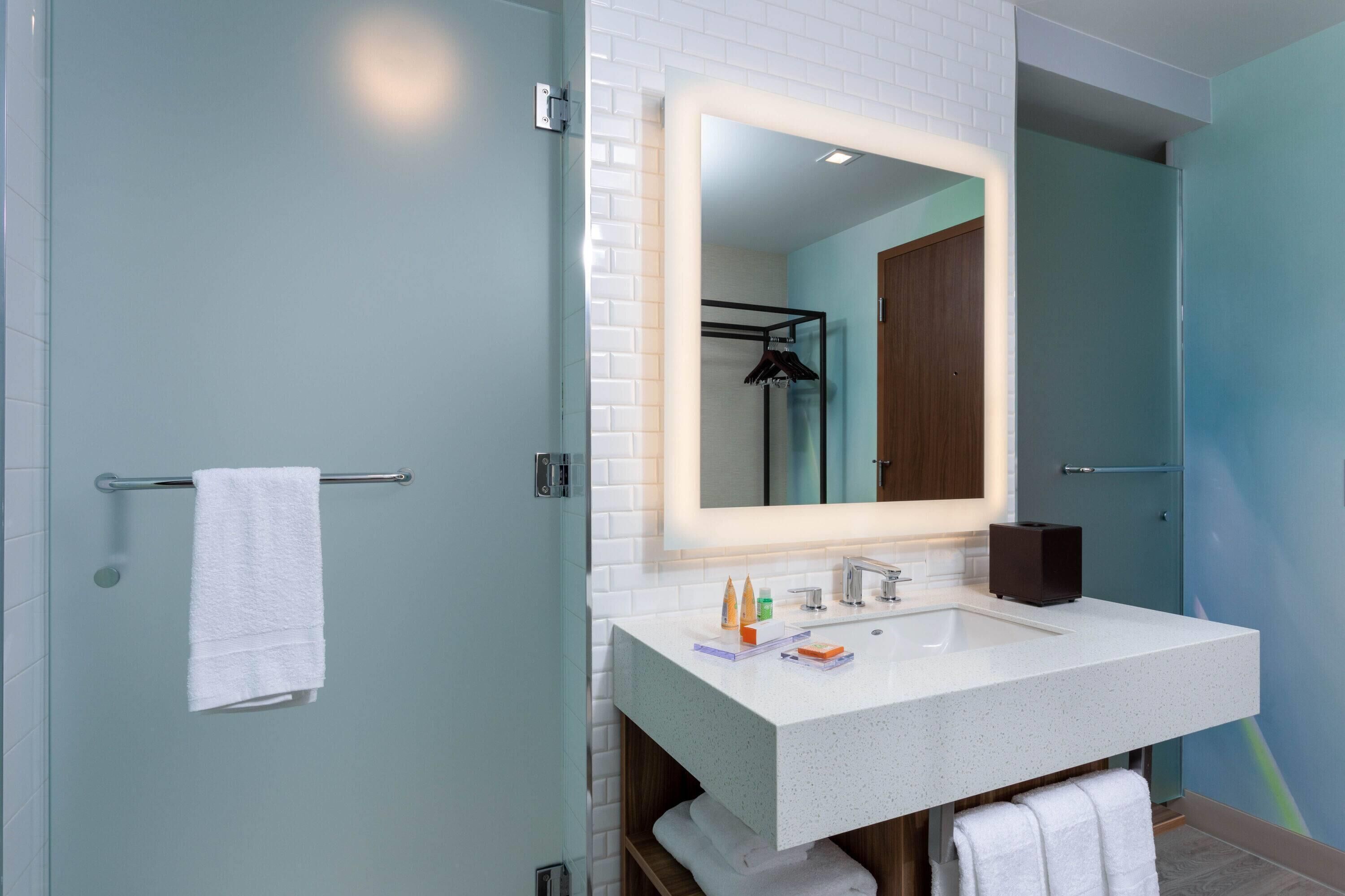 Un baño moderno con un lavabo blanco, un espejo con luz y un perchero para toallas.