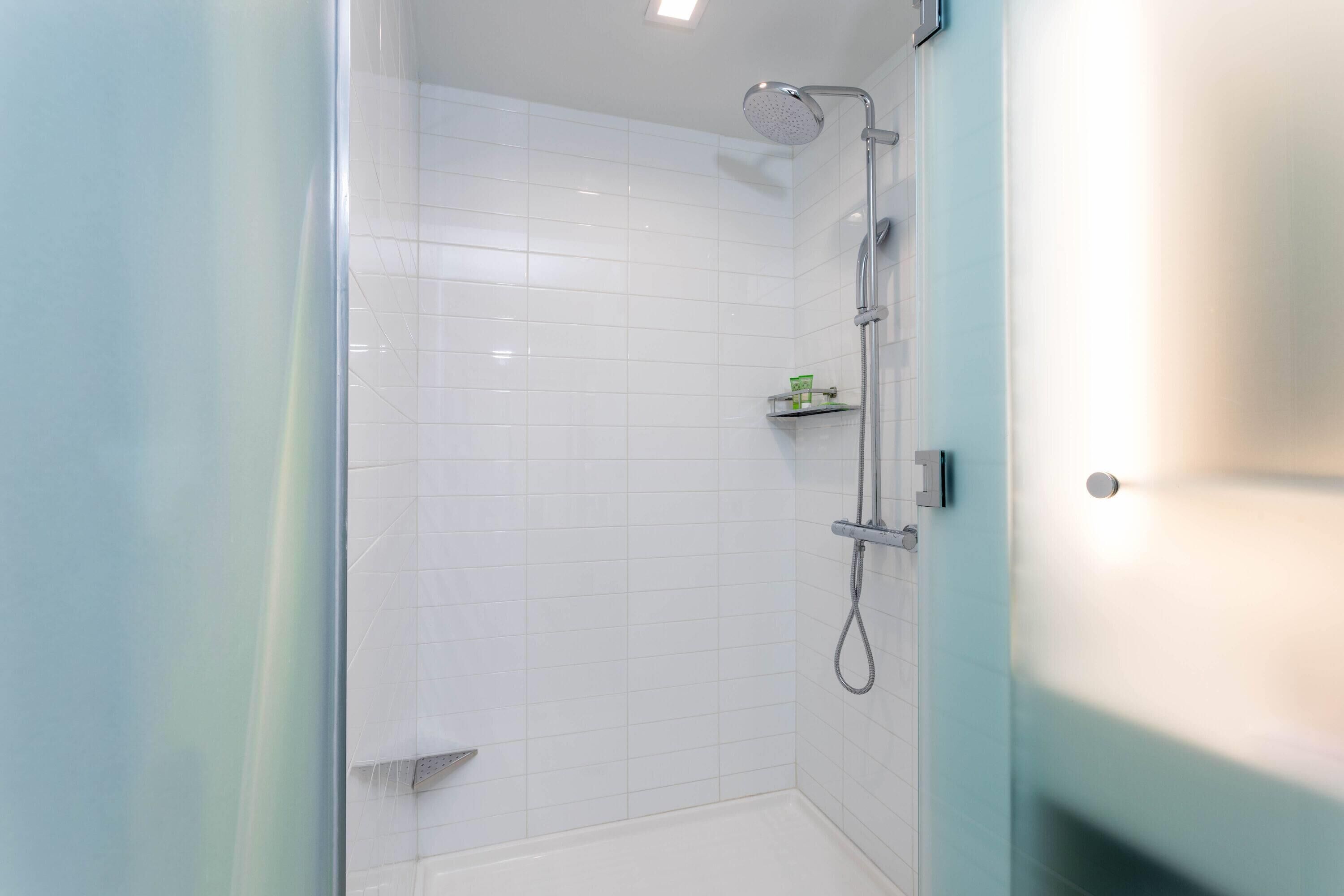 Een moderne badkamer met witte tegels, een douche en een douchecabine met glazen wanden.