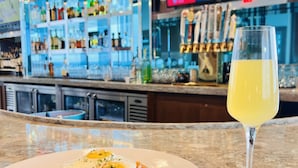 A bar area with a television displaying a sports event, a glass of yellow beverage, and a plate of food with fries and a fried egg. - Wyndham Garden Miami International Airport (Miami Springs)