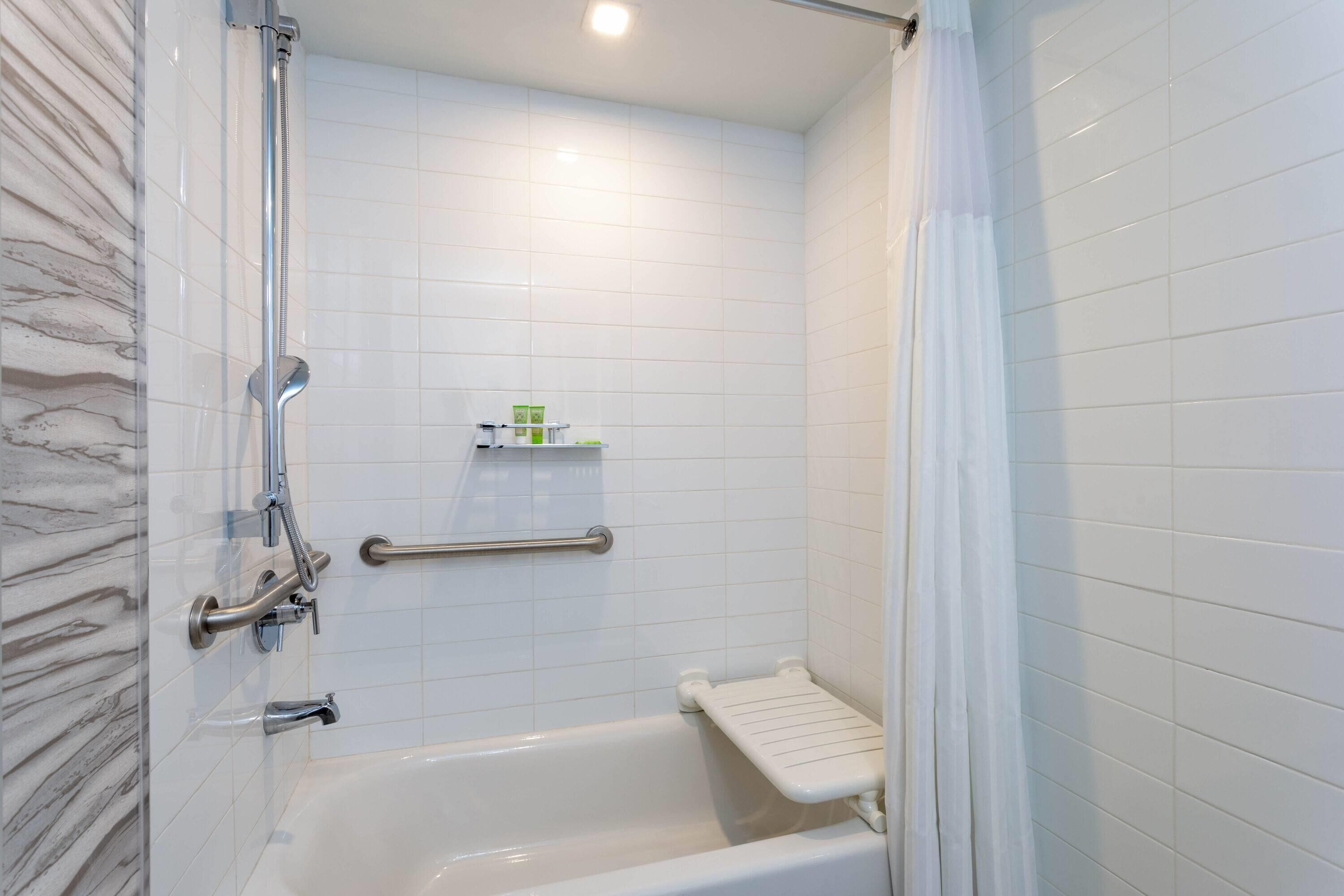 A bathroom with a bathtub, a shower, and a handrail.