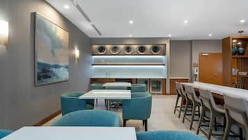 Un moderno hall de hotel con comedor, un cuadro grande y zona de bar.
