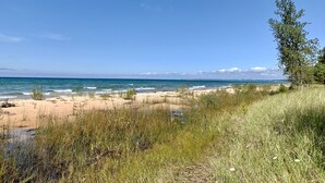 En strand med klare himmel, sandet bredde og sparsom vegetation.