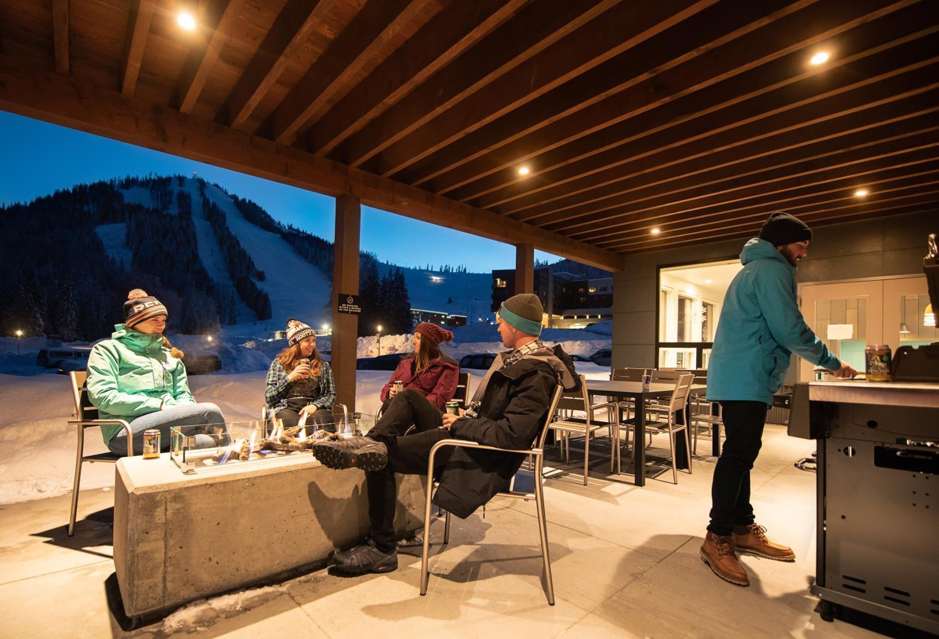 Un espacio de estar al aire libre con techo y vista a una montaña nevada al anochecer.