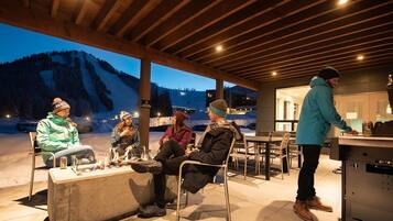 Un espacio de estar al aire libre con techo y vista a una montaña nevada al anochecer.