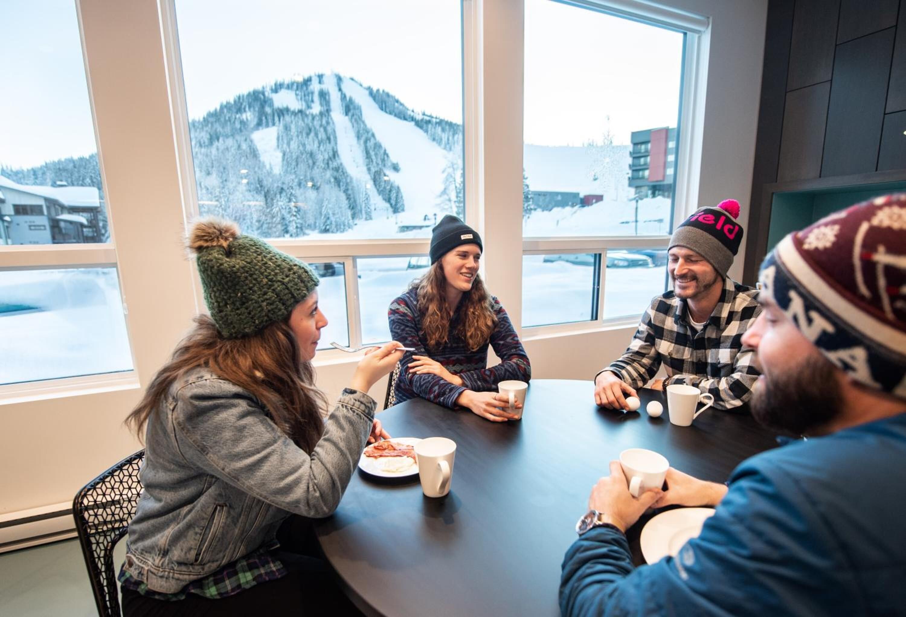 A group of people sitting around a table in a room with large windows overlooking a snowy mountain landscape.
