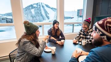 A group of people sitting around a table in a room with large windows overlooking a snowy mountain landscape.