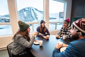 A group of people sitting around a table in a room with large windows overlooking a snowy mountain landscape.