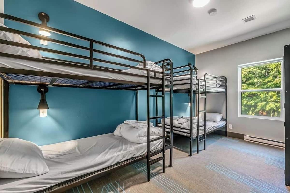 Un dormitorio con literas, tres literas, una ventana con vistas a la vegetación y una lámpara en el techo.