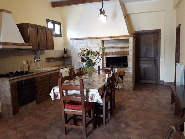 A kitchen with a dining table, chairs, a fireplace, and wooden cabinets.