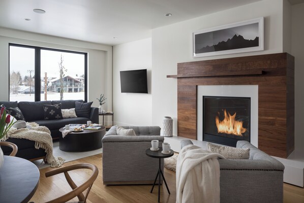 A modern living room with a fireplace, a large window, and a flat-screen TV.