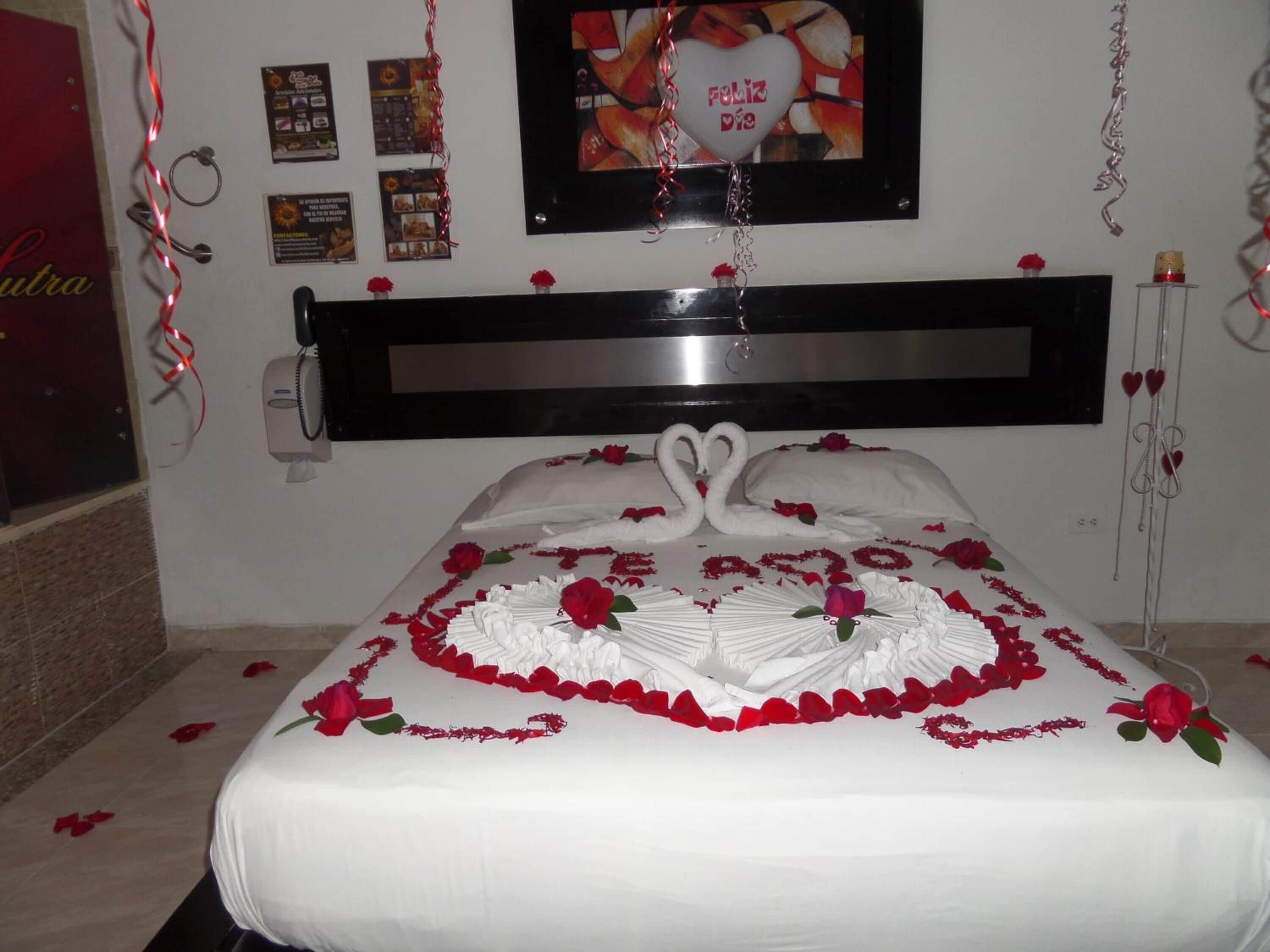 A bed with a white bedspread, red roses, and swan-shaped pillows.