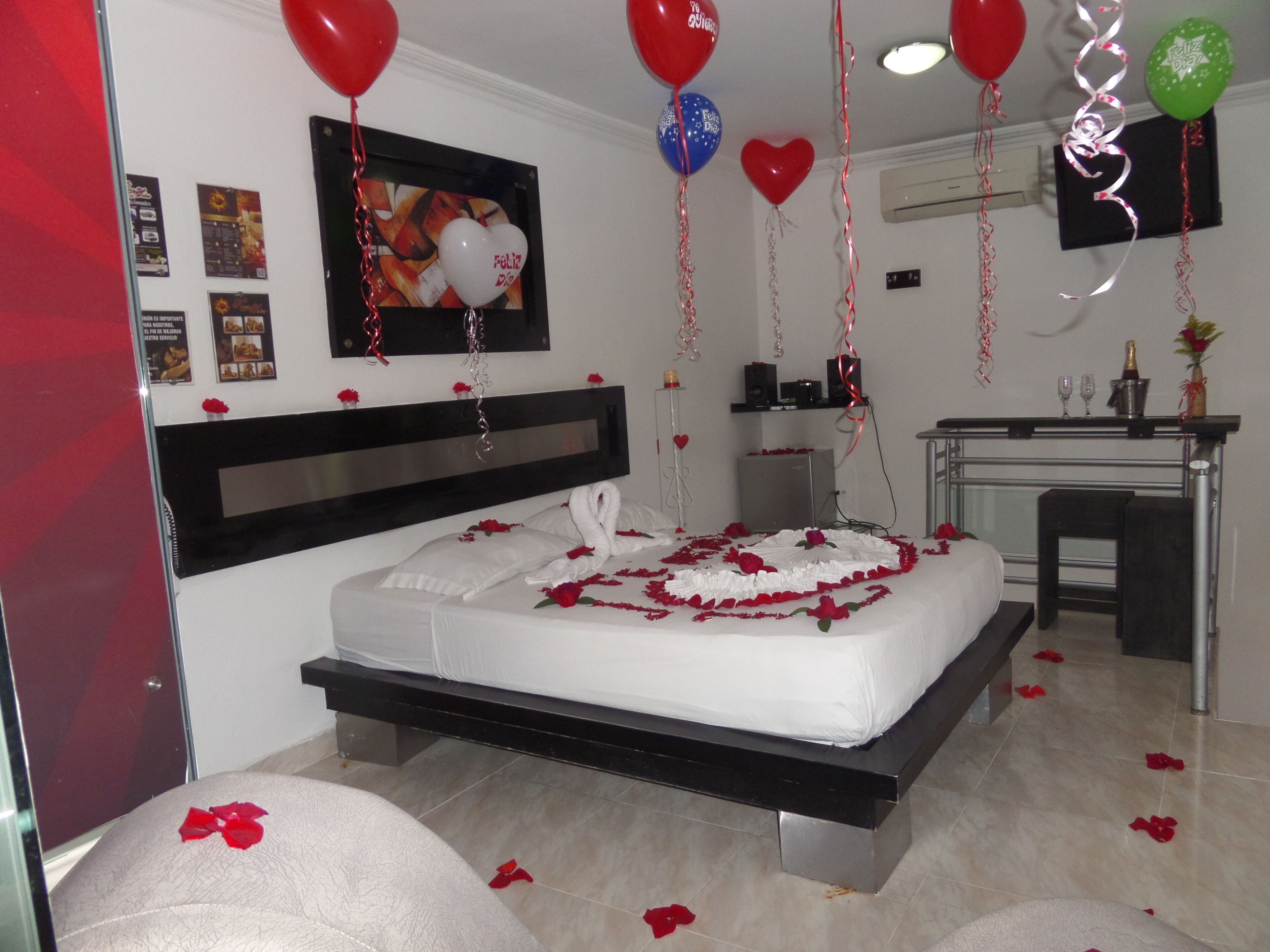 Habitación de hotel con cama, escritorio y una silla. Hay globos y un cuadro en la pared.