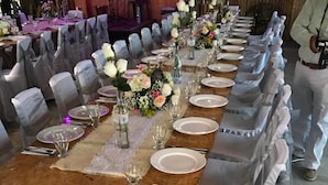 A long banquet table set with white plates, glasses, and cutlery, flanked by chairs with grey covers. - Torettos (Yumbo)