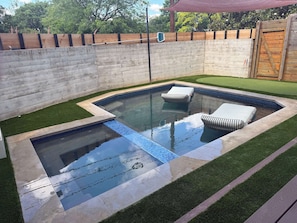 A rectangular swimming pool with two lounge chairs, surrounded by artificial grass and a concrete wall.