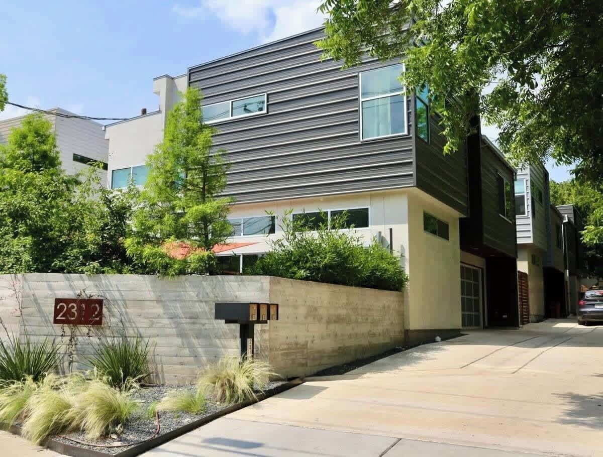 A modern multi-story residential building with a stone wall, a mailbox, and a clear sky.