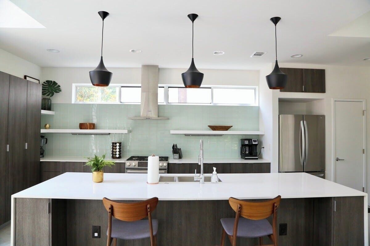 A modern kitchen with a large island, pendant lights, and stainless steel appliances.