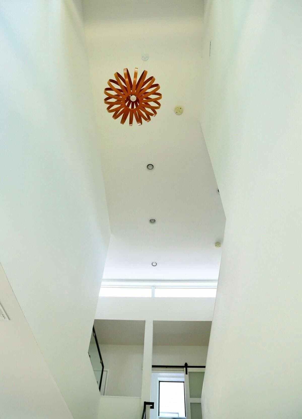 Techo alto con un detalle decorativo naranja, iluminación empotrada y vista de una escalera que sube a otro nivel.