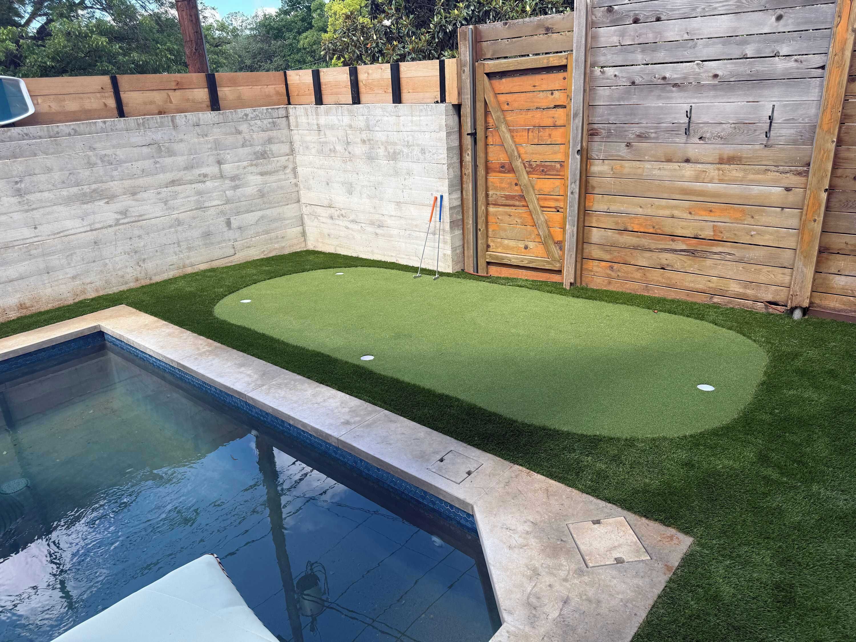 Una piscina con una zona de césped artificial, una valla de madera y un muro de madera.