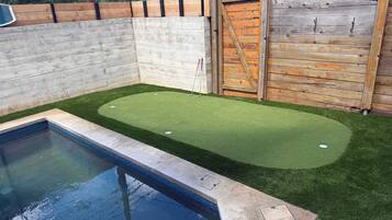 Una piscina con una zona de césped artificial, una valla de madera y un muro de madera.