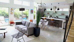 Et moderne opholdsområde med åbent planløsning, indeholdende sofa, spisebord med stole, et køkken med bar samt en trappe.