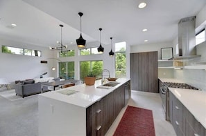 A modern kitchen with a central island, pendant lighting, and a view of the outdoors.