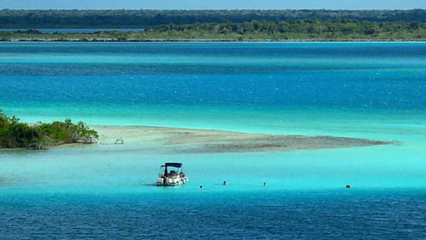 Un barco en un mar turquesa con una playa y una zona boscosa al fondo.