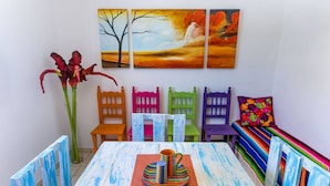 Un comedor con una mesa dispuesta para dos personas, sillas coloridas y un banco con cojín floral.