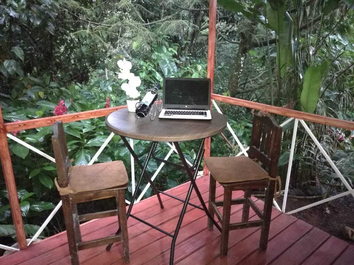 Una terraza de madera con una mesa redonda y dos sillas, una computadora portátil y una cámara sobre la mesa.