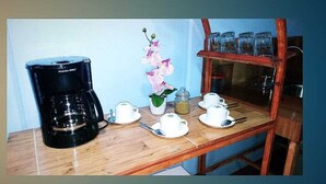 A wooden table with a coffee maker, teapots, cups, and a flower vase.