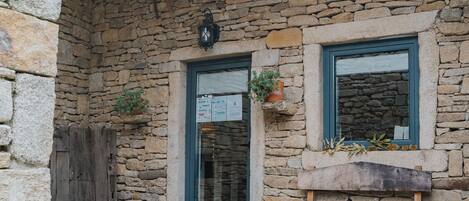 A stone building with a wooden bench, a lantern, and a window with a plant.