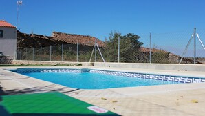 A swimming pool with a tiled edge, a fence, and a building with a tiled roof in the background.